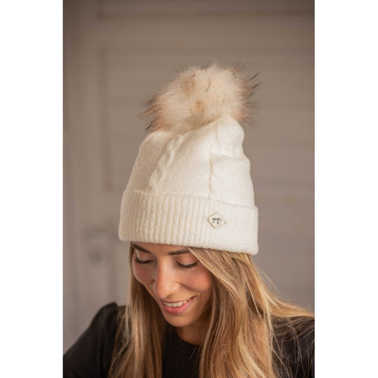 Penelope Michka cable knit pom-pom hat with wide cuff and diamond-shaped logo plate.