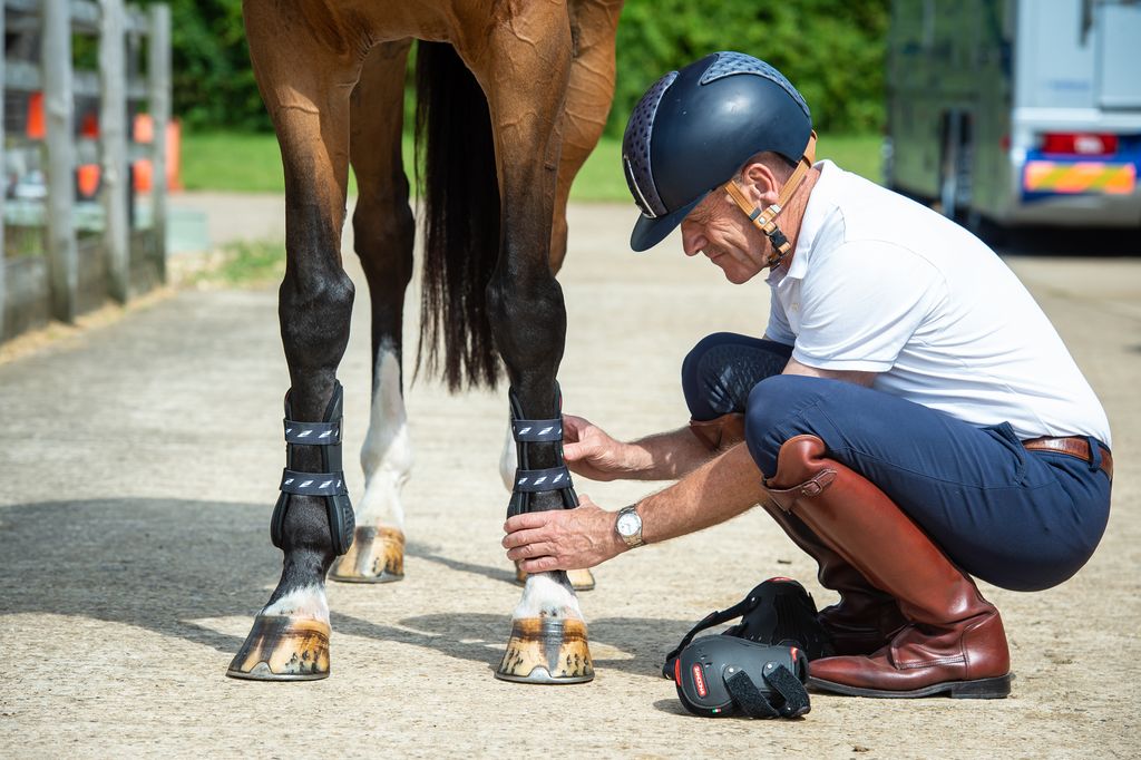 Andrew Hoy putting a Zandona Tendon boot on his brown horse, wearing a Kep Italia Helmet