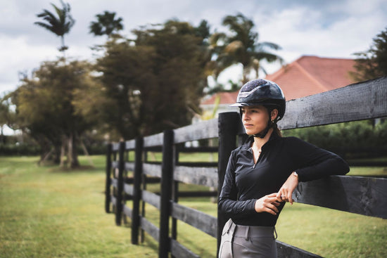 Lady equestrian wearing a black Kask star lady helmet with Swarovski leaning on a wooden field fence
