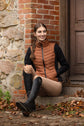 Woman sitting on steps wearing a kingsland brown puffer vest and checked breeches